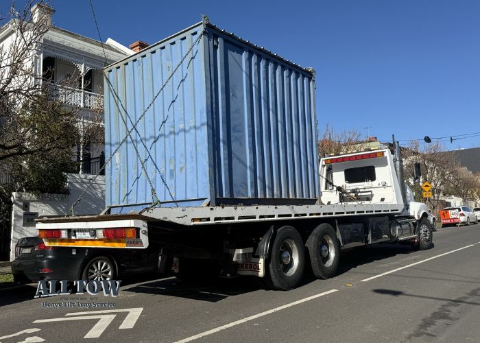 Tilt tray truck delivering blue shipping container in Melbourne suburb