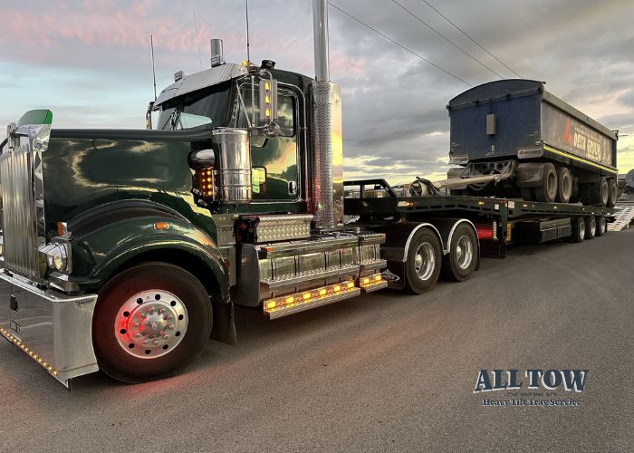 Kenworth tilt tray truck towing heavy vehicle trailer at sunset in Melbourne