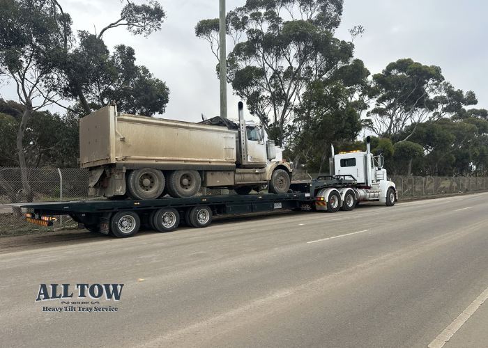 White Kenworth tilt tray towing large dump truck on Melbourne road